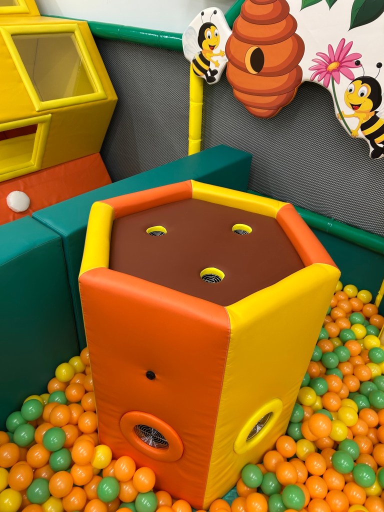 A padded installation in the ball pit with three holes for air to flow upward and balls to hover in the air stream.